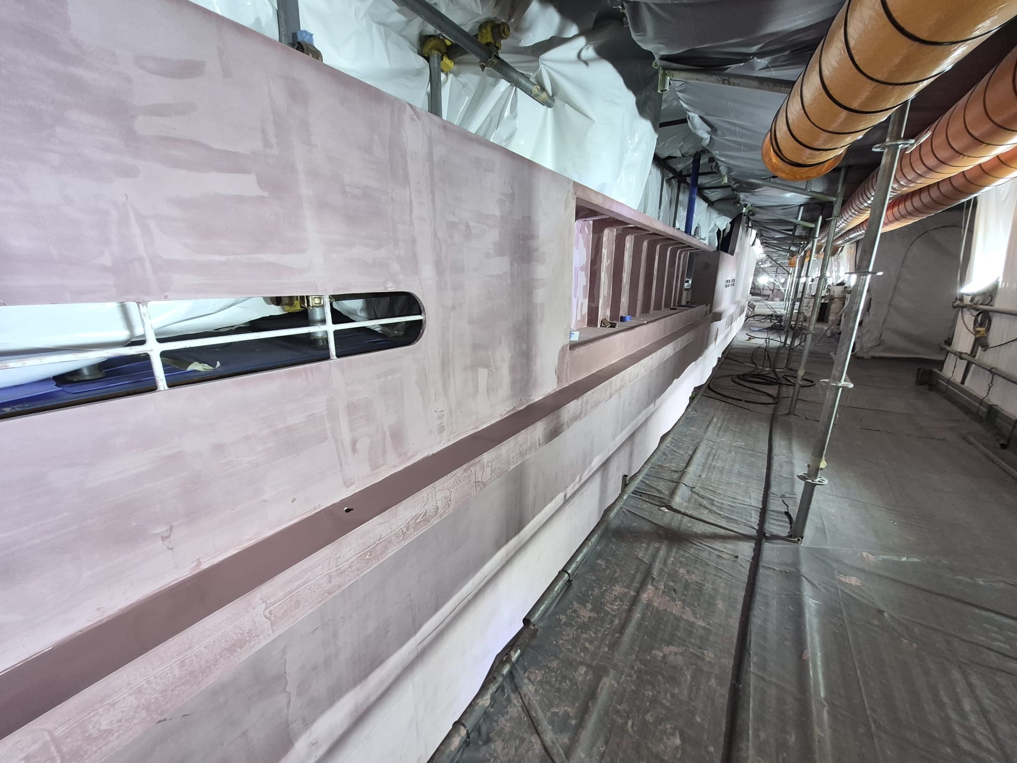 Faired hull side in the tented scaffold walkway on a 76.6 m explorer yacht refit, Singapore
