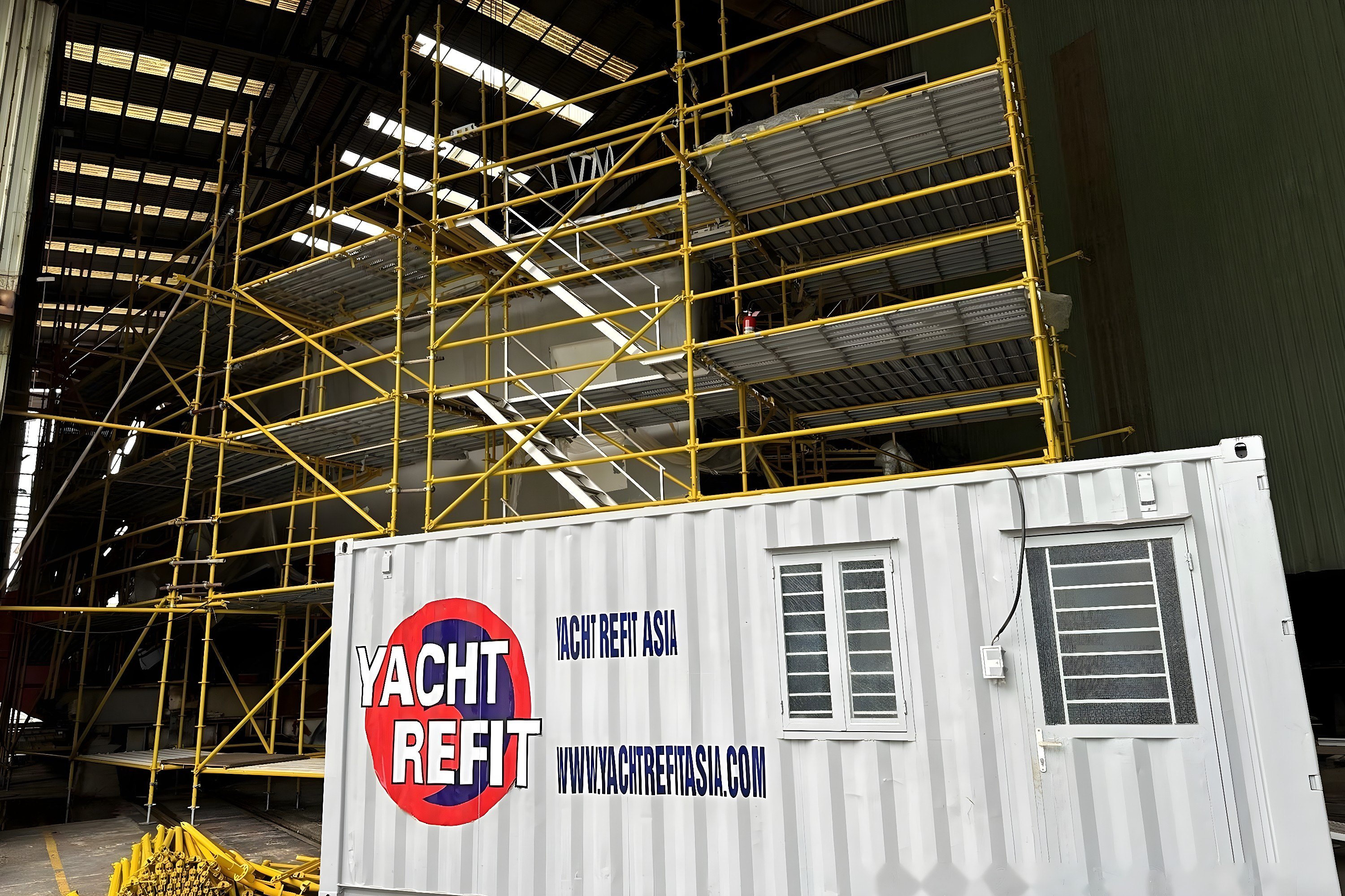 White site container in front of scaffolding around one 33 m hull in the Haiphong shed